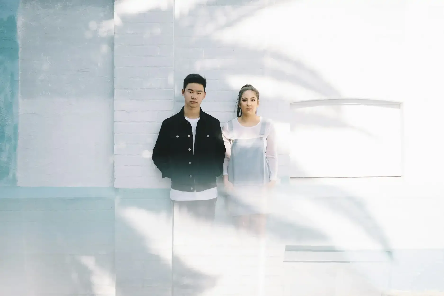 interracial couple standing next to each other against a white brick wall