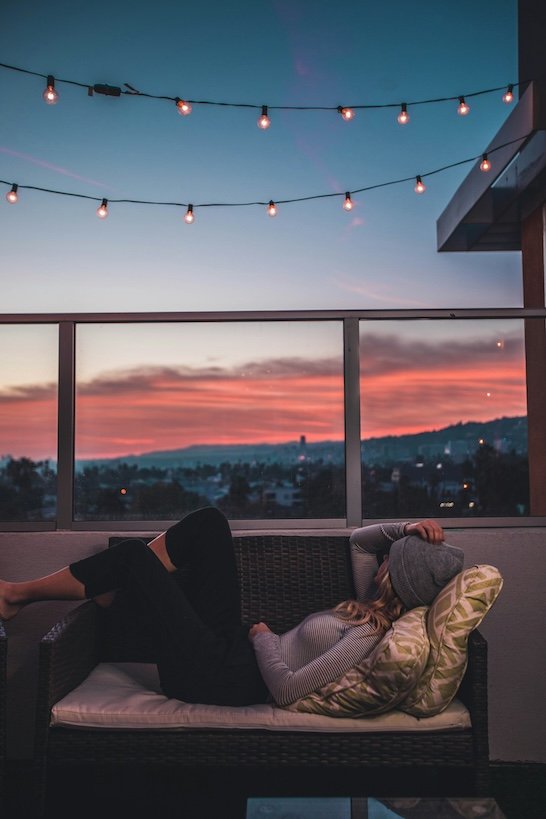 young woman laying on a bench on a porch at sunset