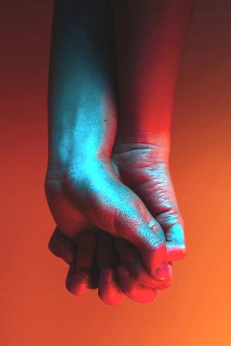 picture in blue and red tones. zoomed in photo of  hands holding each other