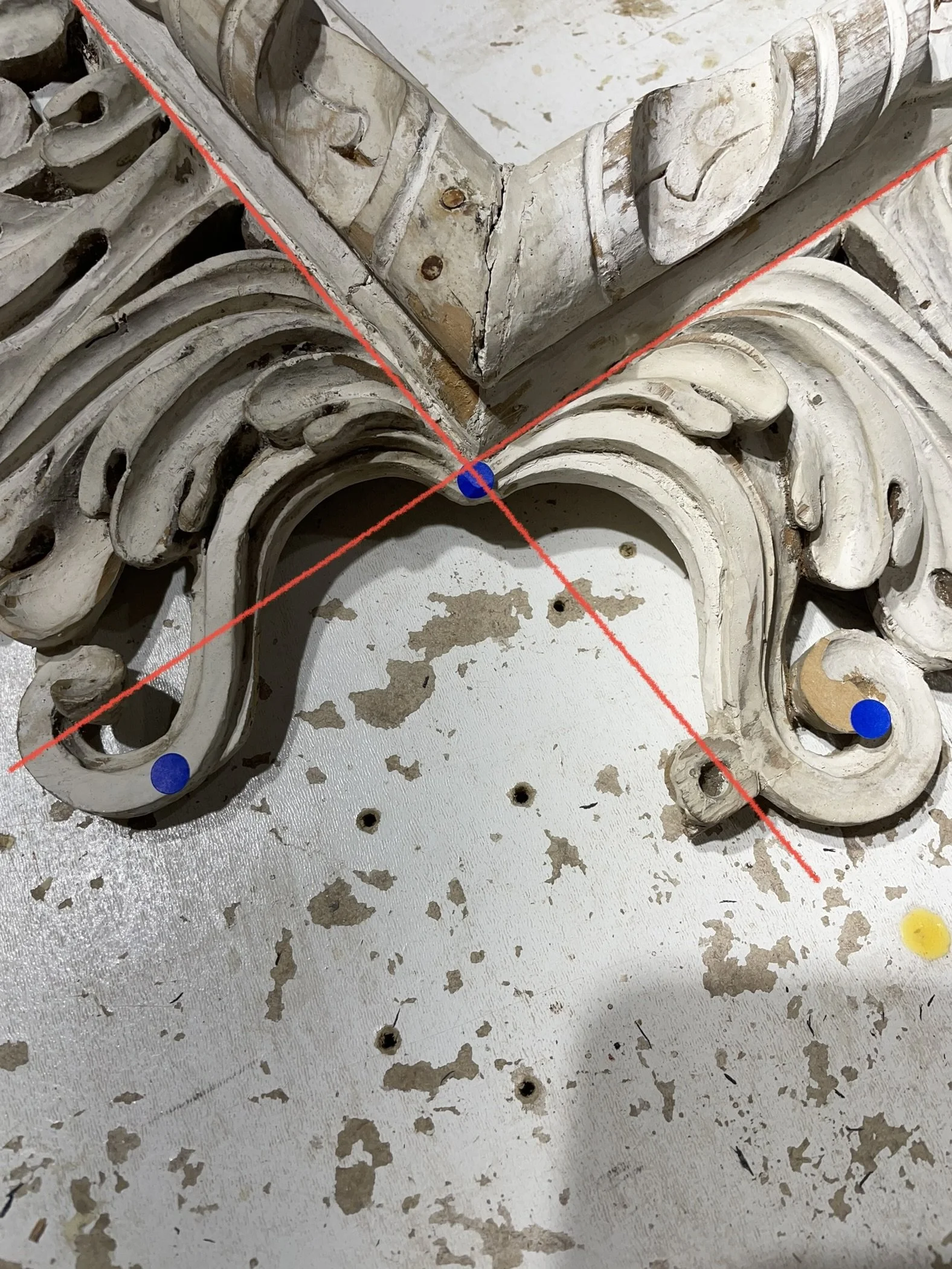 A decorative wooden frame with intricate carvings, lying on a distressed white surface with some scattered holes and paint peeling.