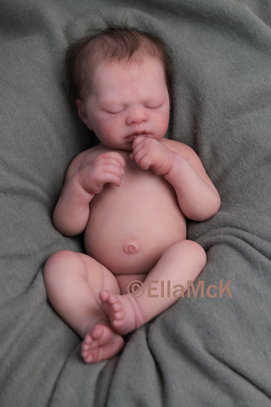 Newborn baby girl sleeping on a patterned blanket, wearing a white onesie with pink bow and butterfly designs, a pink knit hat, and covered partially with a white blanket.