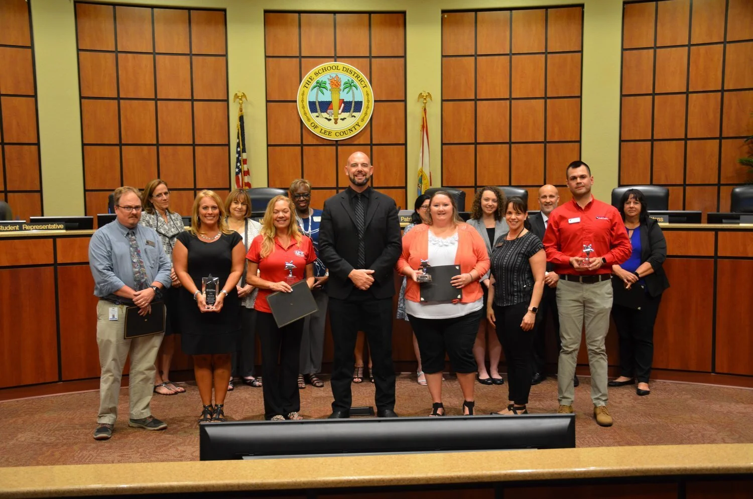 Award ceremony at the School District of Lee County boardroom with educators and officials posing with certificates and trophies.