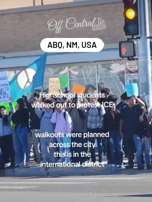 High school students protesting ICE in Albuquerque, standing at a street corner with signs and flags.