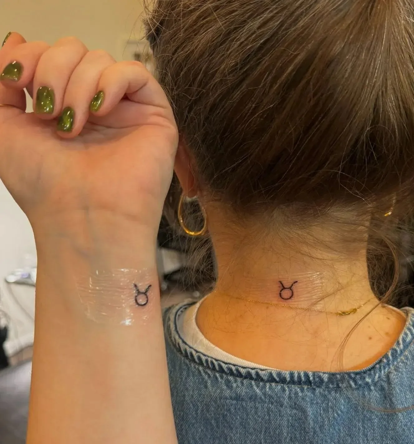 Close-up of matching Taurus symbol tattoos on a wrist and the back of a neck.