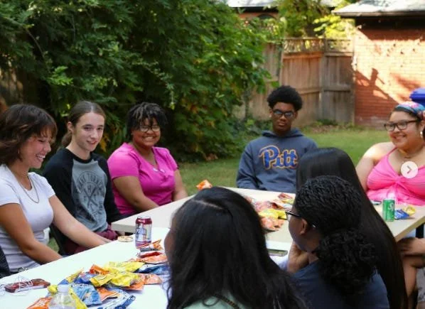 Group of students gathered around a table with snacks, smiling and talking during a youth voter event.