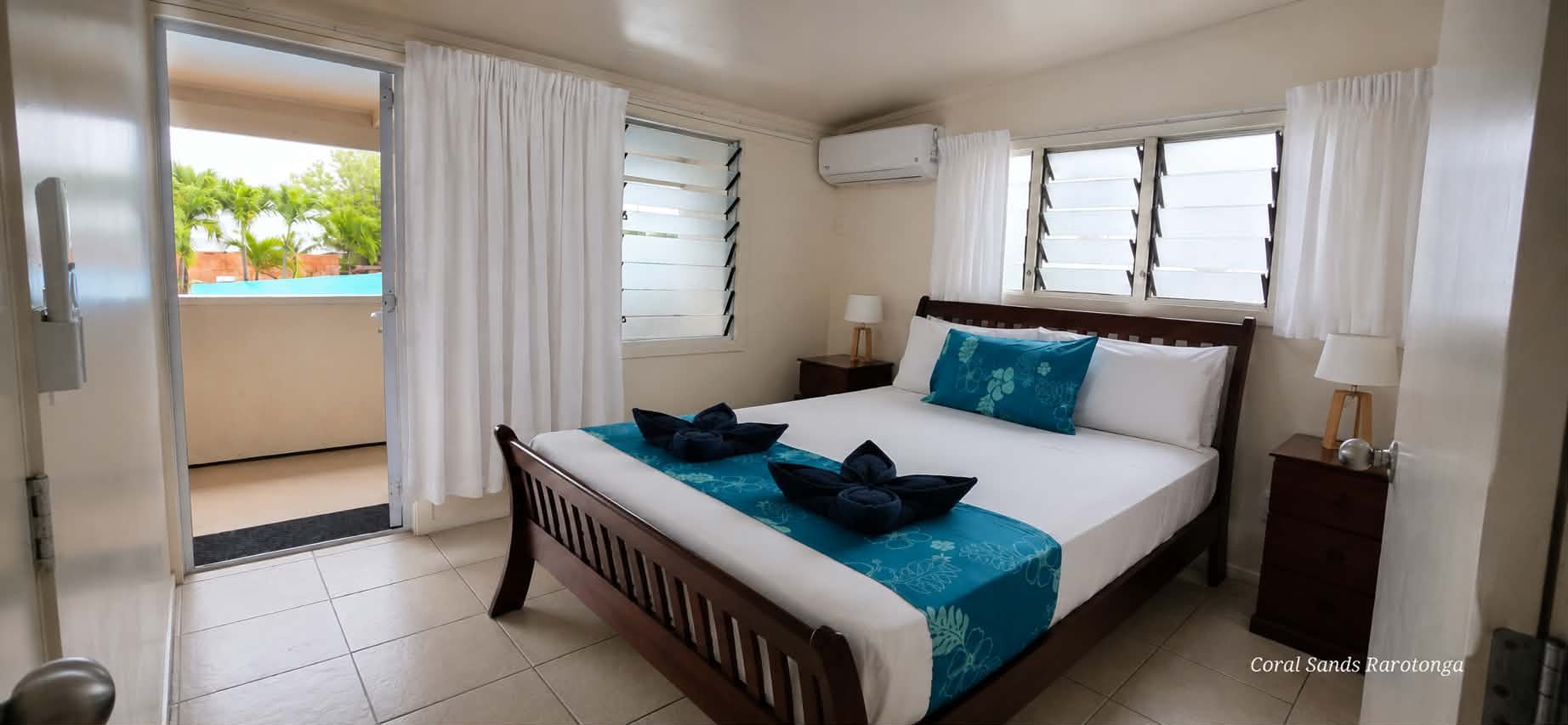 Upstairs bedroom in the Three Bedroom Apartment at Coral Sands Apartments in Arorangi, Rarotonga, featuring a queen bed, tropical décor, air conditioning and pool views.