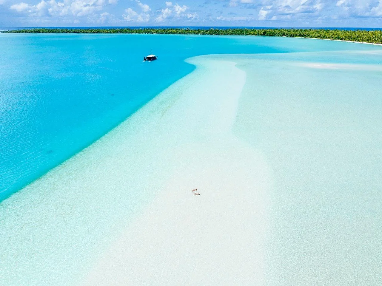 Visitors relaxing on a pristine sandbank surrounded by the crystal-clear turquoise waters of Aitutaki Lagoon, Cook Islands.