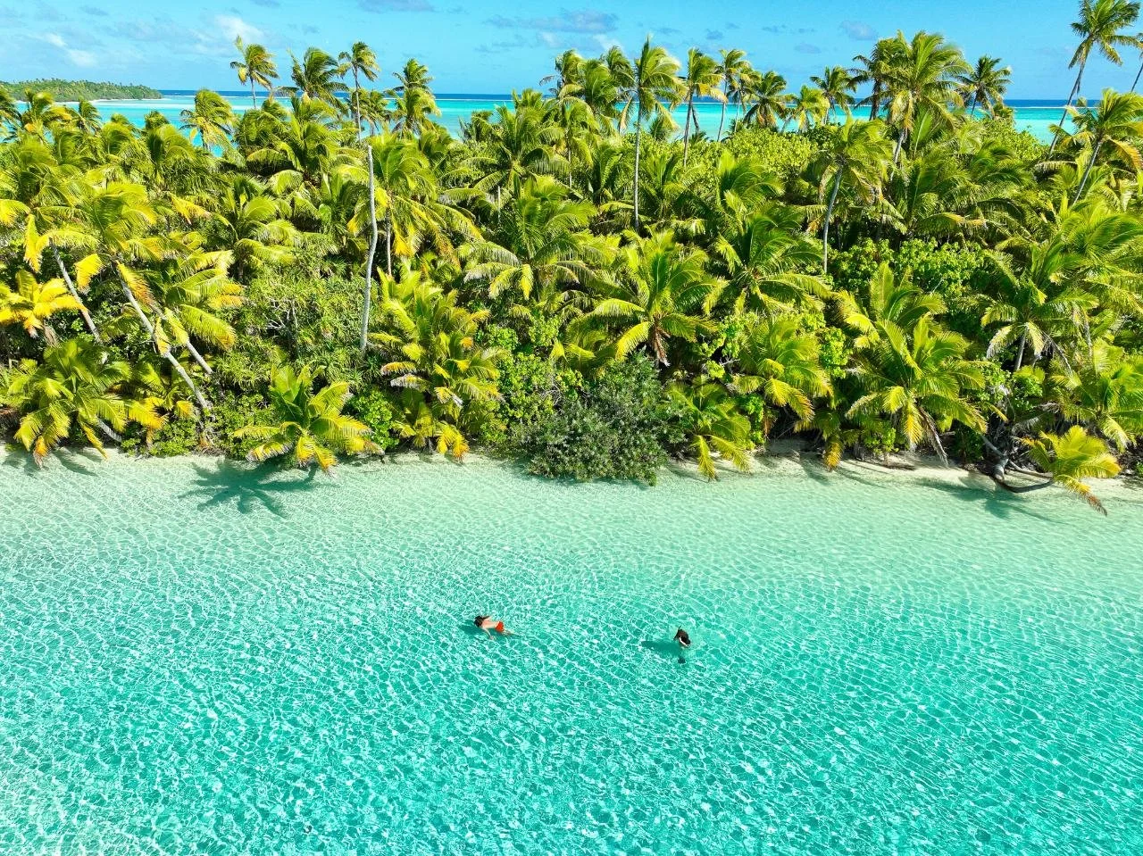 Visitors swimming in the crystal-clear lagoon beside One Foot Island in Aitutaki, Cook Islands.