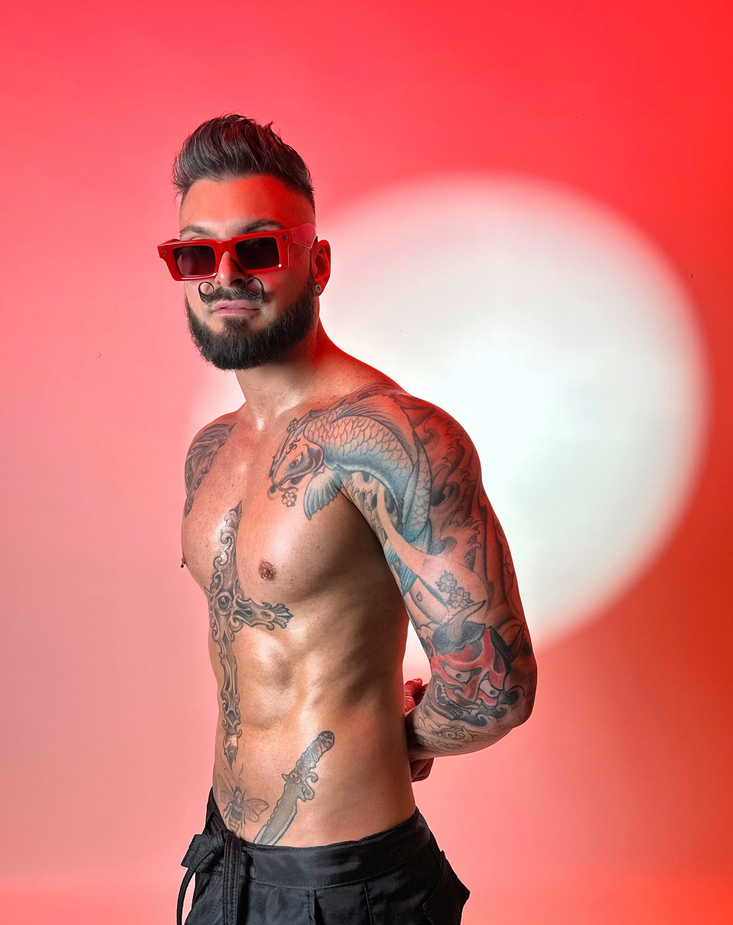 DJ LEOW wearing red sunglasses, with styled dark hair and tattooed shoulders
