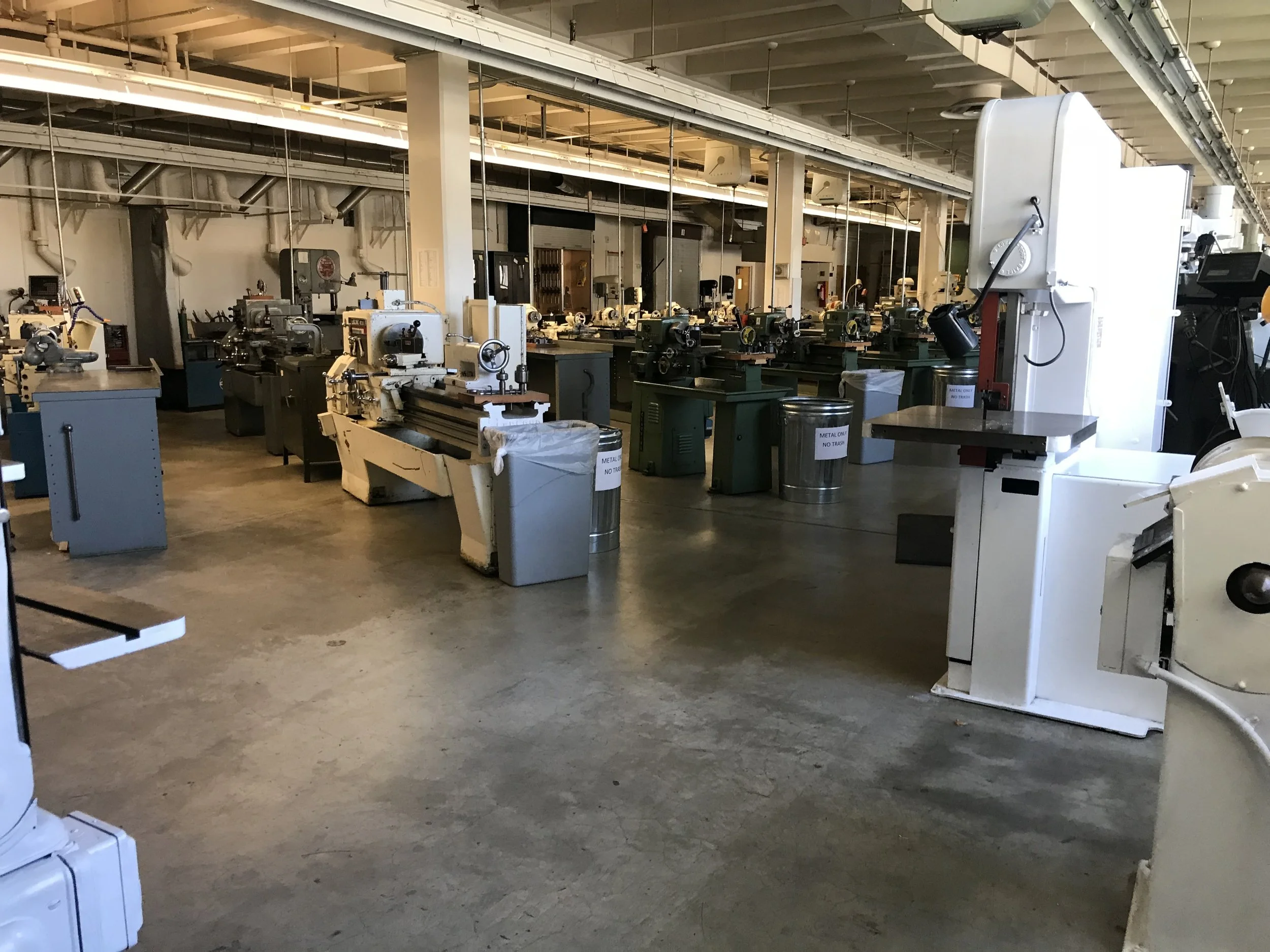 A large industrial machine shop featuring multiple workbenches and machines used for metalworking, with a spacious floor and overhead lighting.