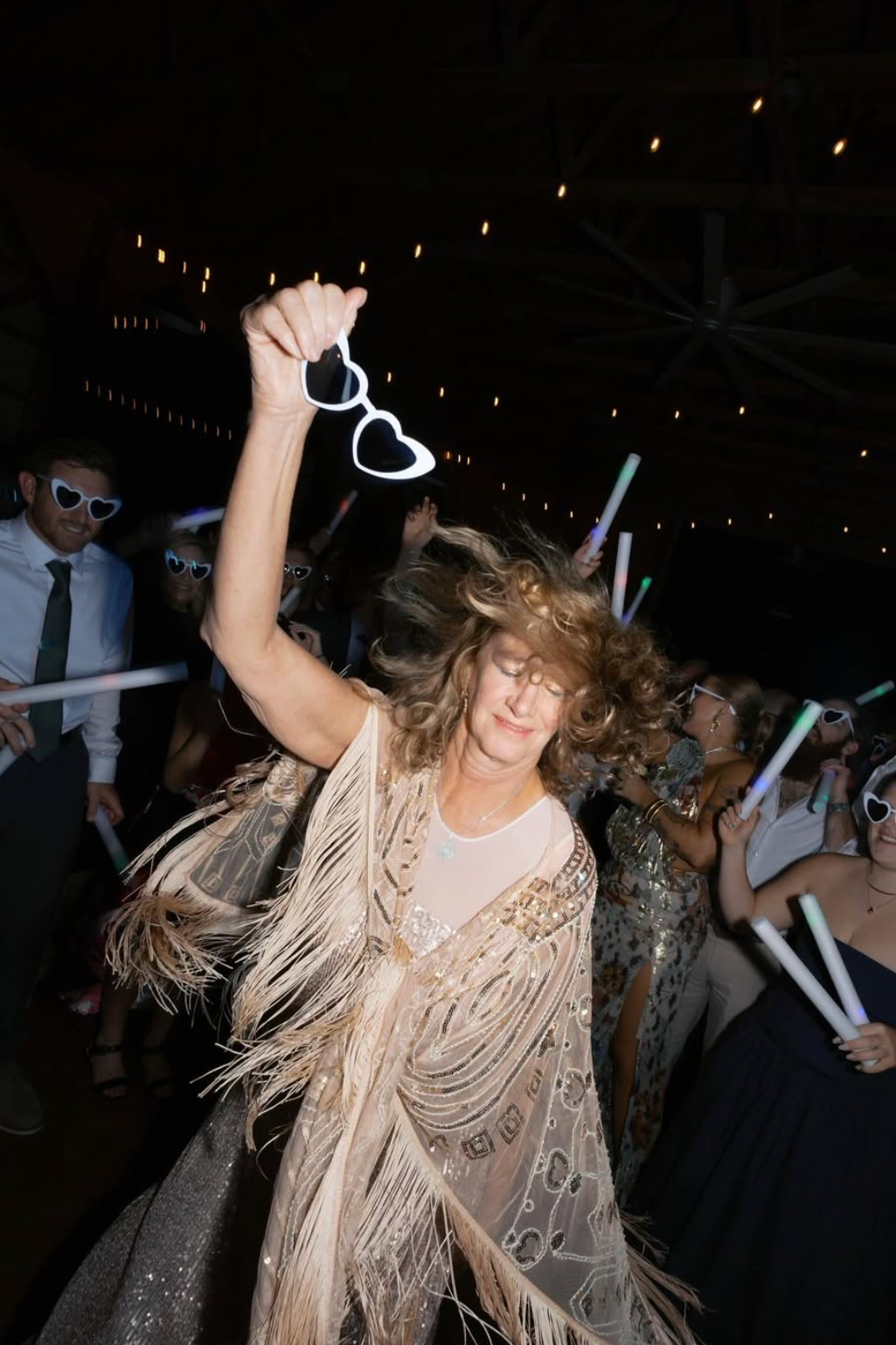 Women dancing at a The Hillside Estate with glow stick glasses, in a dimly lit venue with string lights.