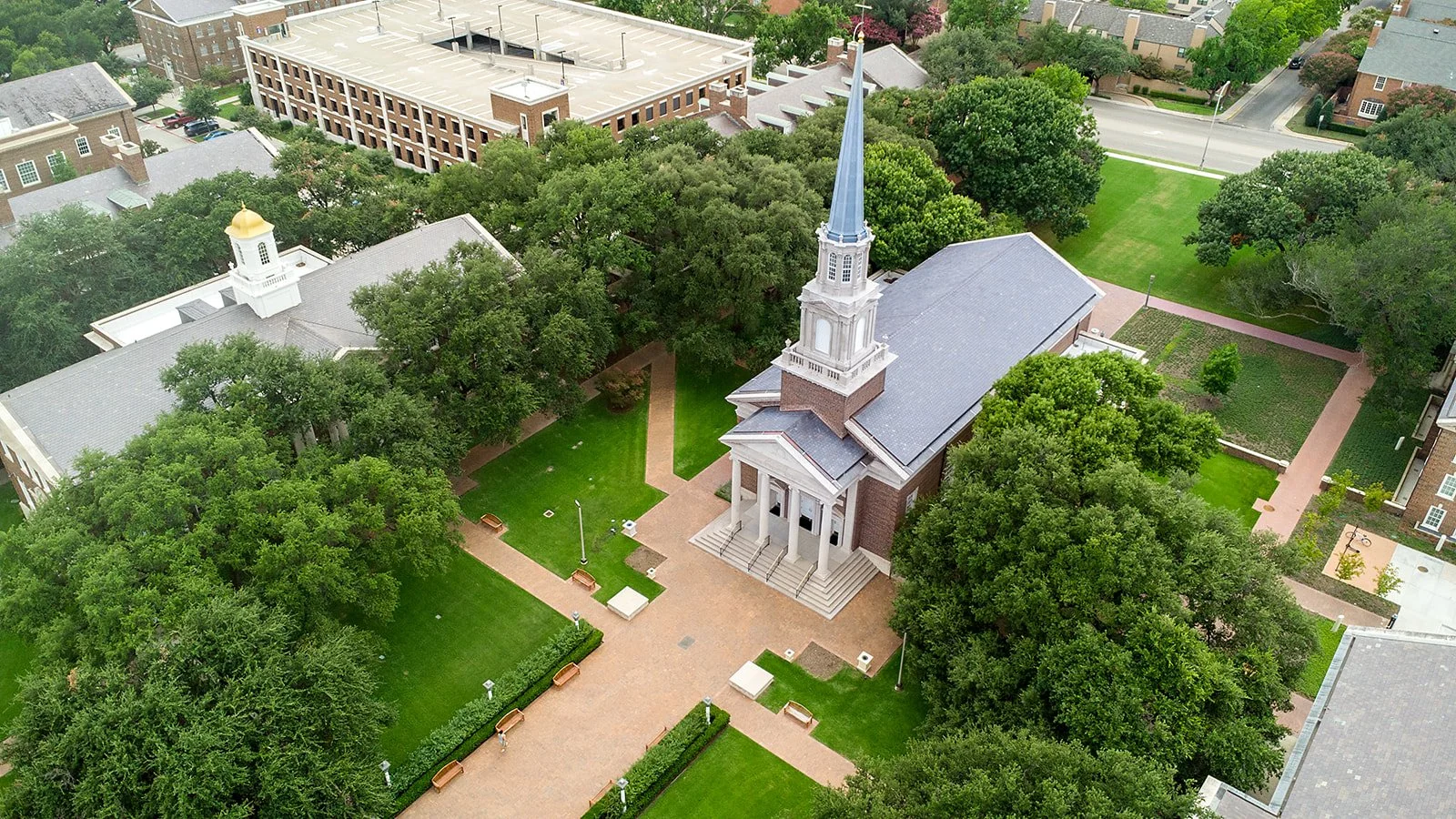 SMU Chapel: Aerial view of a church with a steeple, surrounded by trees, walkways, benches, and nearby buildings.