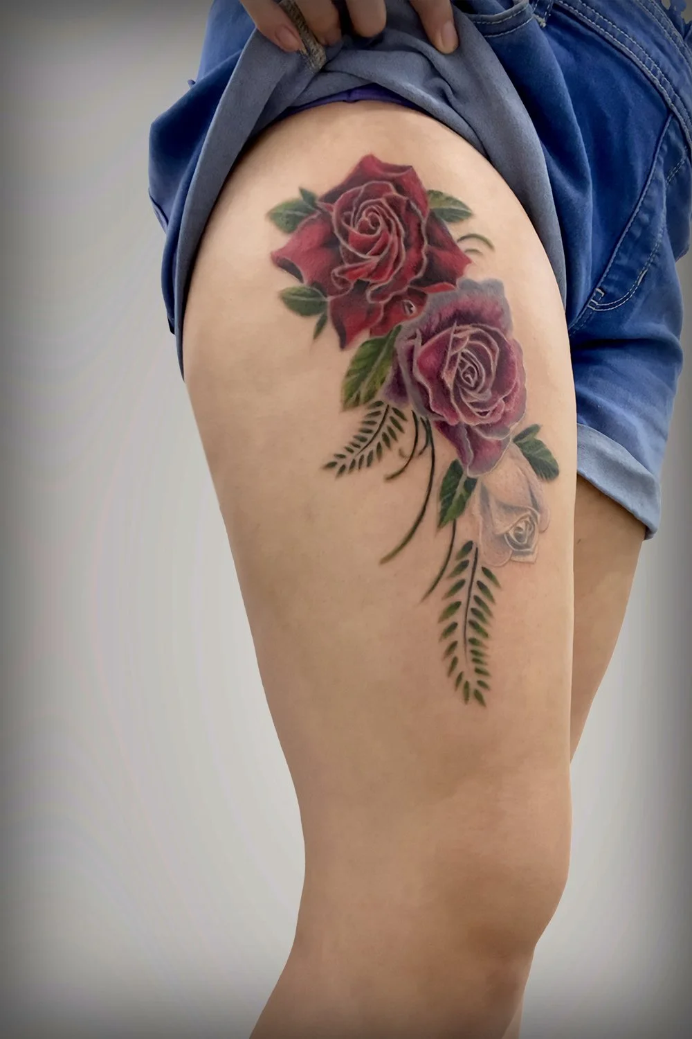 Woman's upper thigh tattoo comprising of three roses, red, pink, and white.