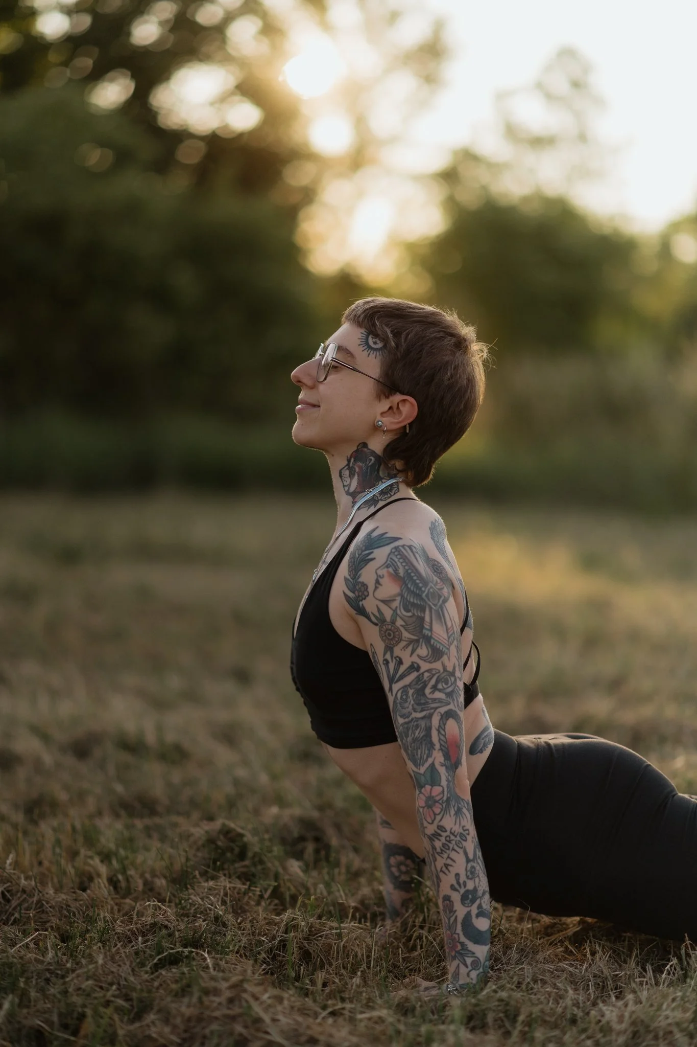 Frau mit Tattoos macht yoga im Freien bei Sonnenuntergang.