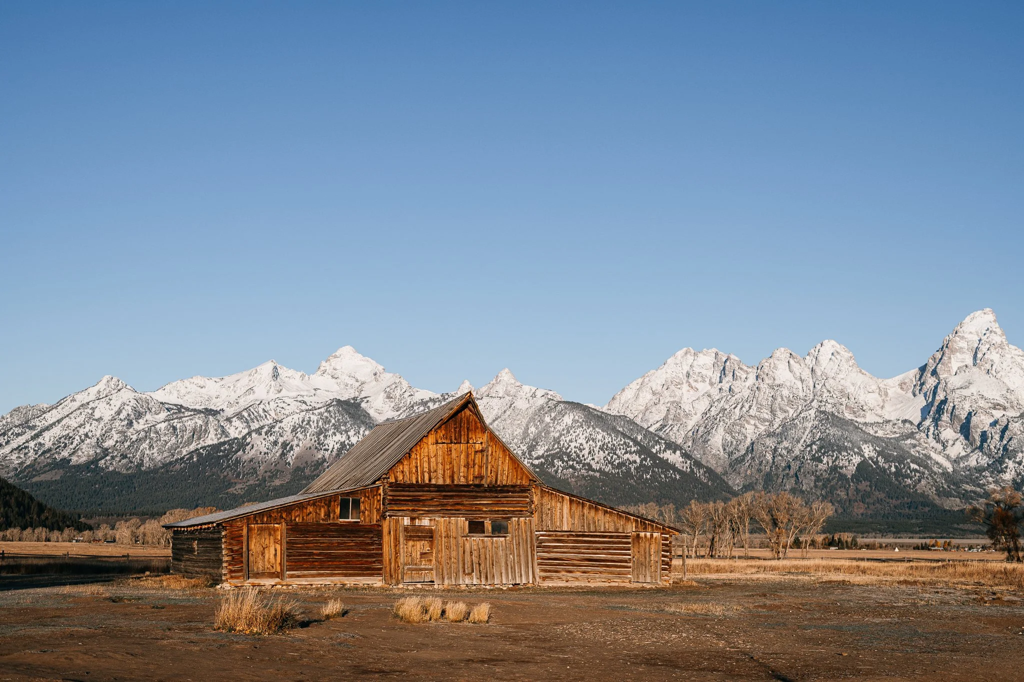 Altes Holzhaus in einer flachen Landschaft mit Bergen im Hintergrund, Schneebedeckte Gipfel, blauer Himmel.