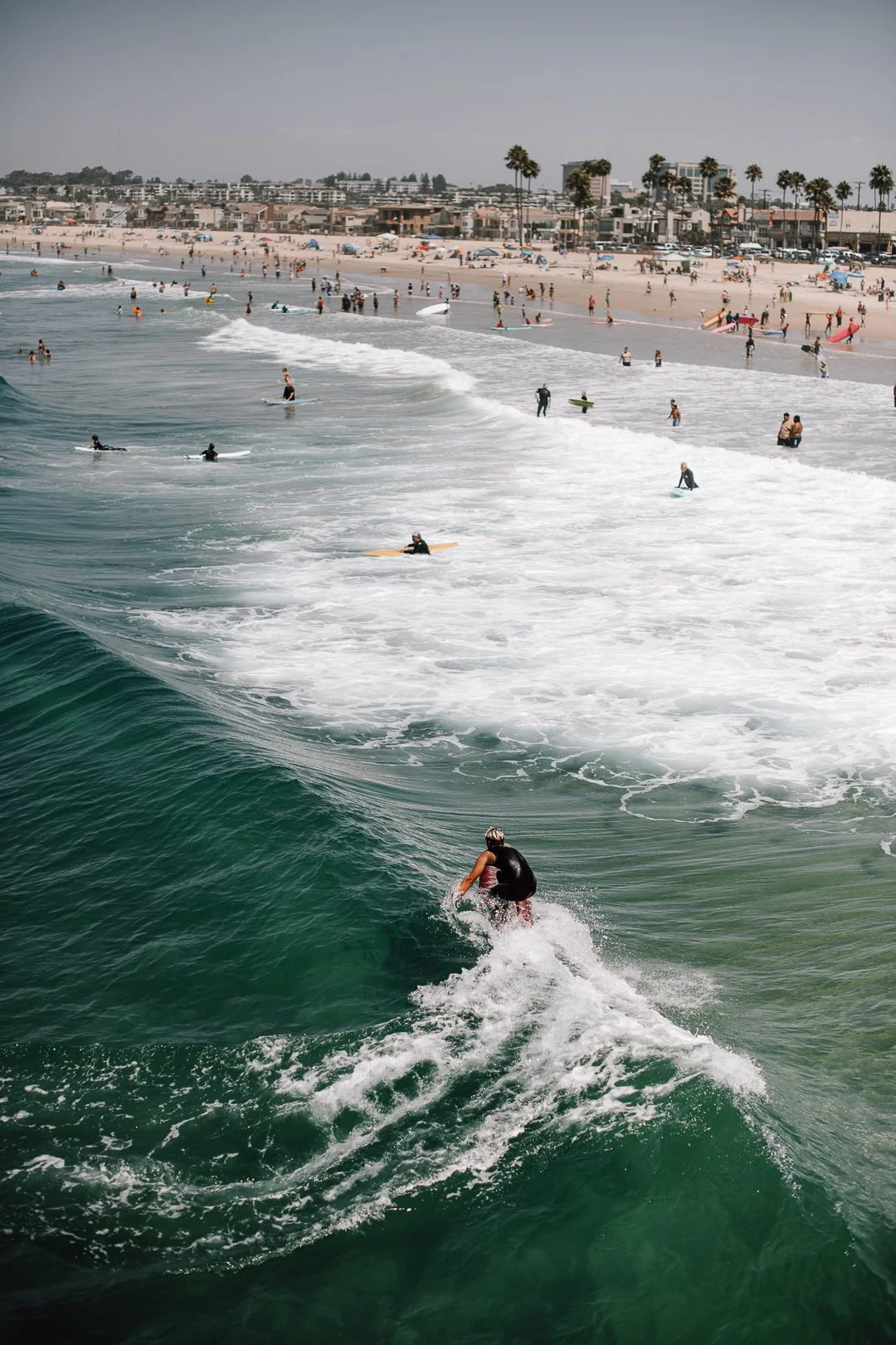 Person surft auf Welle, Strand im Hintergrund – Reisefotografie Meer Kalifornien
