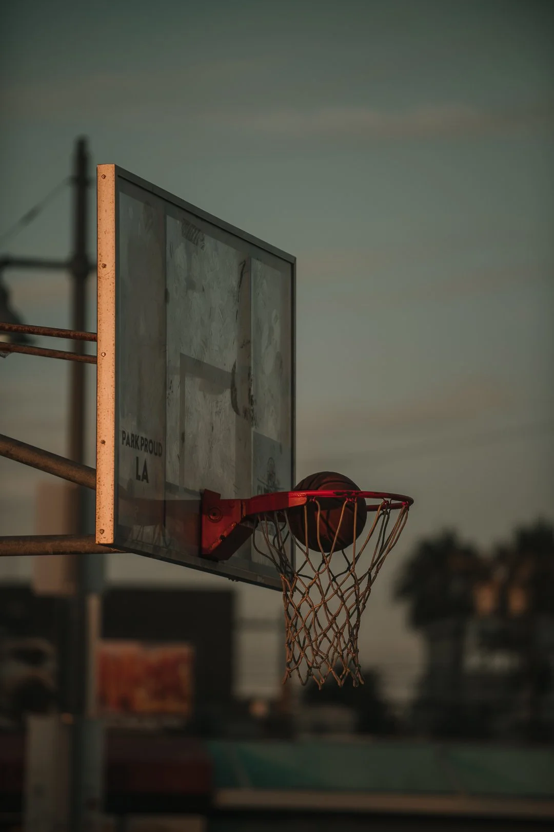 Basketballkorb mit Ball in Sonnenuntergangsstimmung auf einem Basketballfeld.