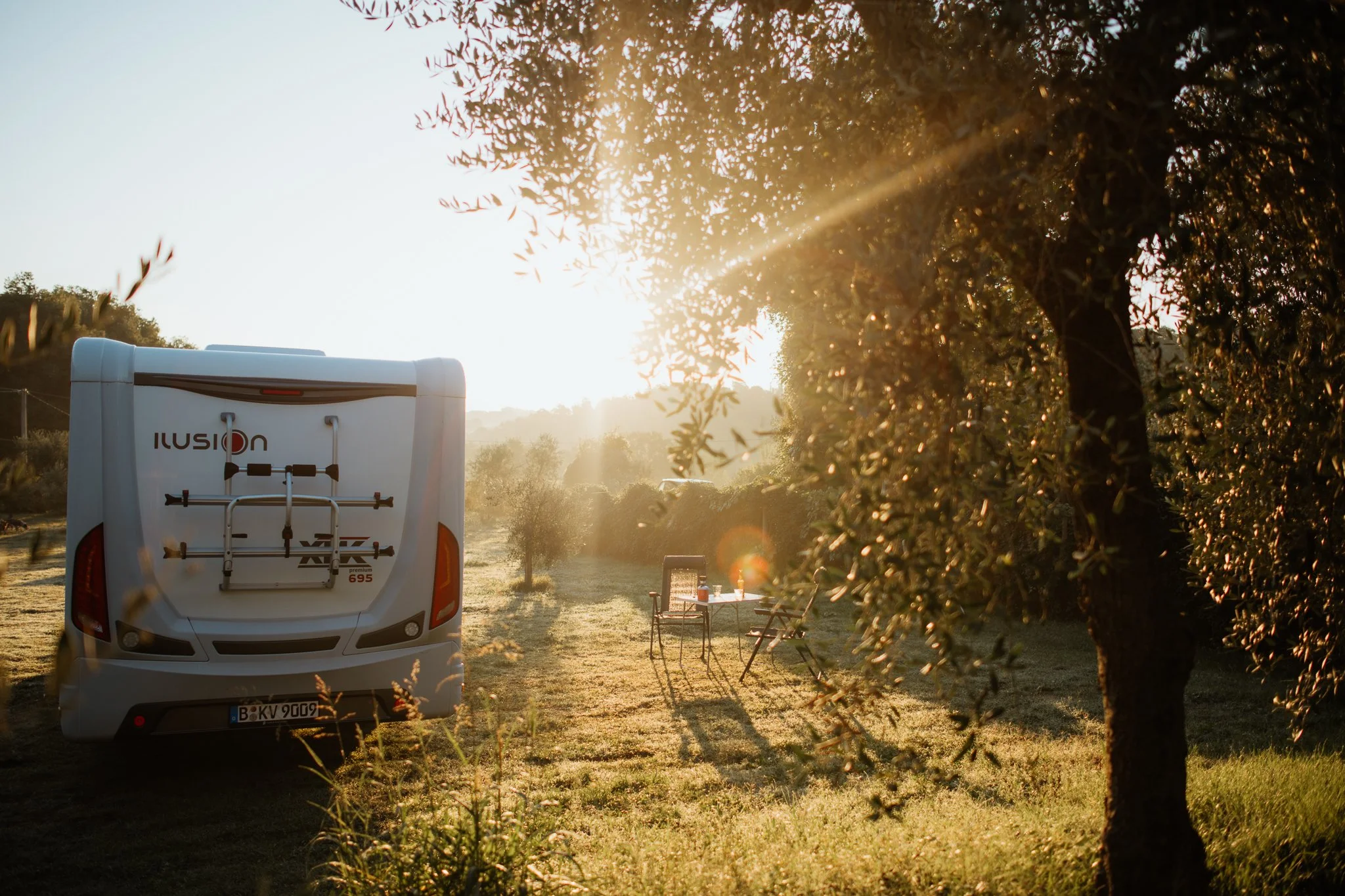 Campingplatz mit Wohnmobil, Tisch & Stühlen im Sonnenuntergang - Tourismusfotografie
