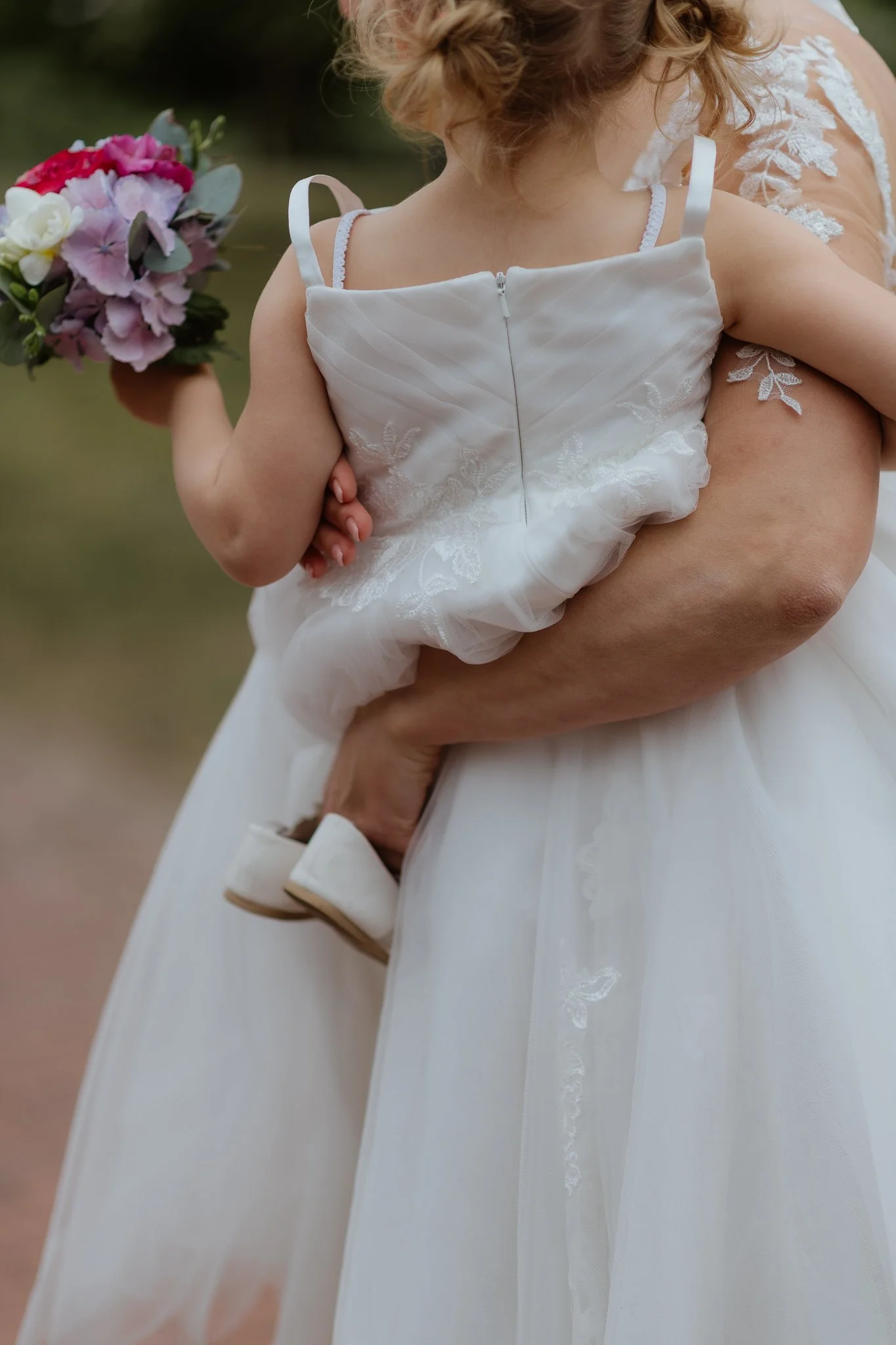 Nahaufnahme eines Kindes in einem weißen Kleid, das von einer Person in einem weißen Kleid gehalten wird, mit einem Blumenstrauß in der Hand.