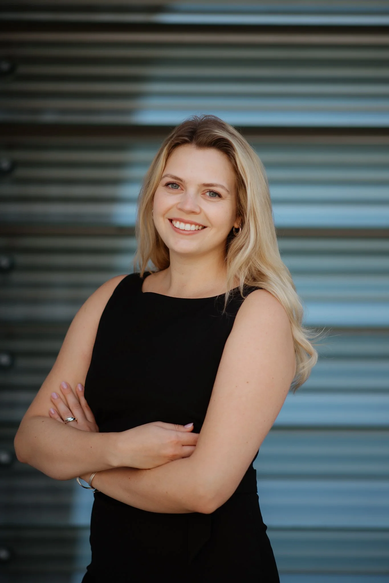 Junge Frau mit blonden Locken lächelnd vor moderner Wand – Business Portraitfotografie Berlin