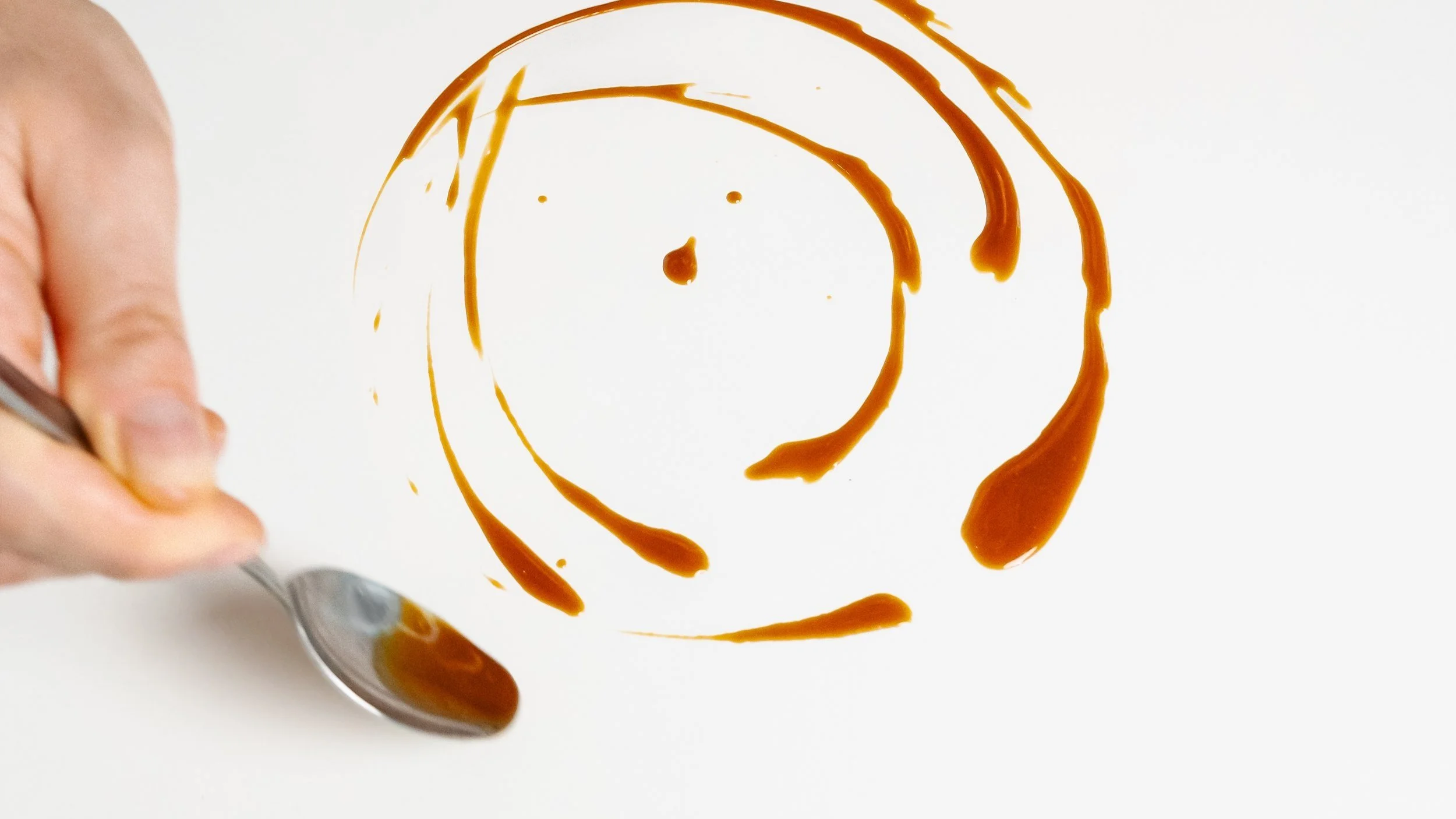Hand holding spoon with sauce, swirled on plate, abstract pattern