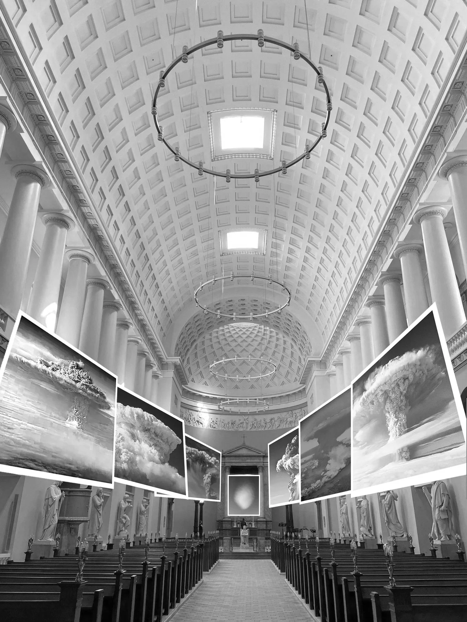 Interior of a grand neoclassical hall with a high, coffered ceiling, white columns, and statues lining the walls. There are large black-and-white photographs of explosions or clouds hanging in the center.