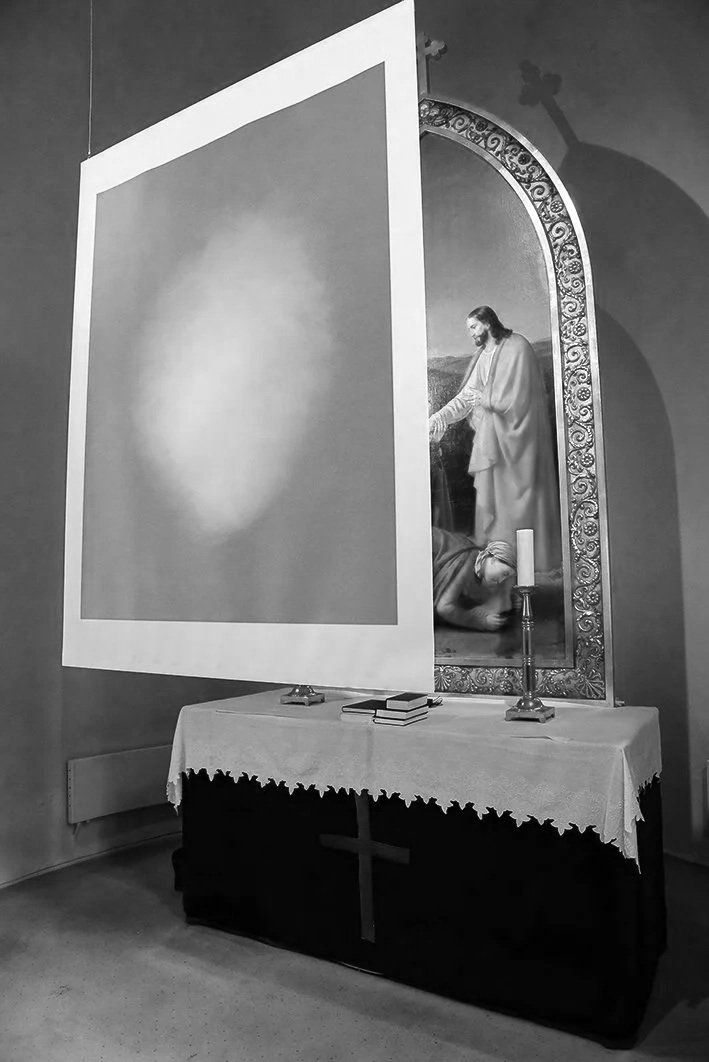 A religious altar with a painting of Jesus, a candle, and prayer books, partially obscured by a large movable screen.