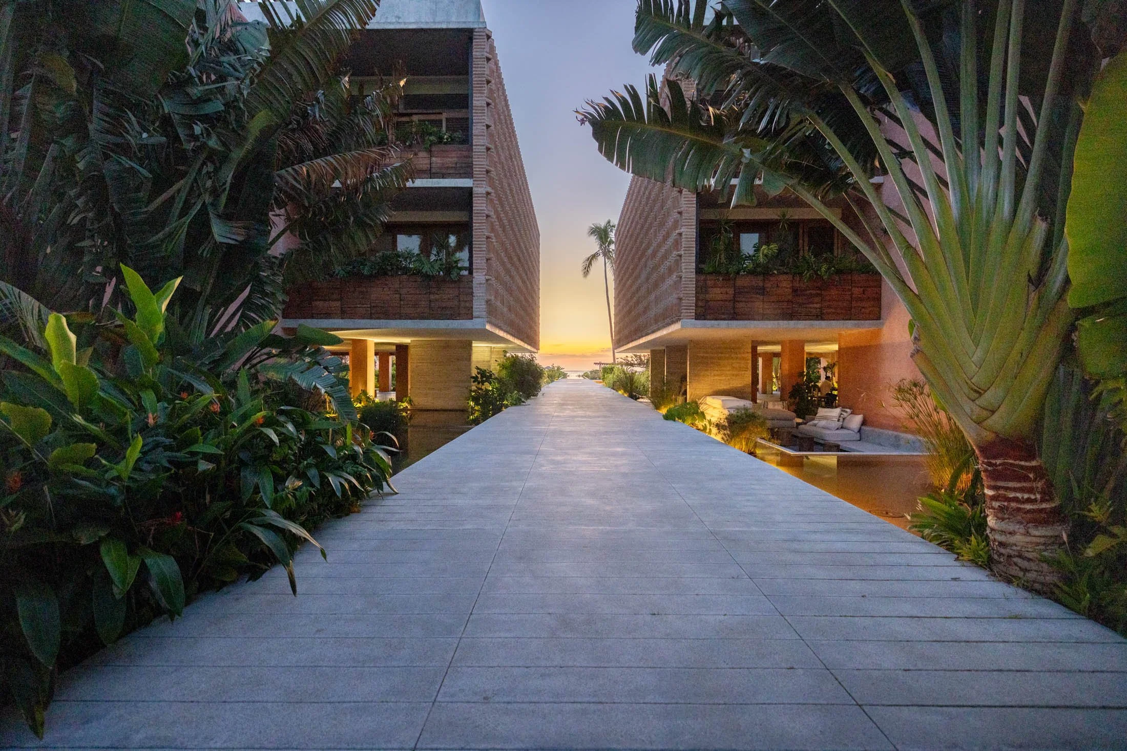 Fotografía arquitectónica del Hotel Careyes en Jalisco, México, donde las palmeras y la cálida luz del atardecer envuelven la estructura del edificio, destacando su elegante diseño en un ambiente sereno.