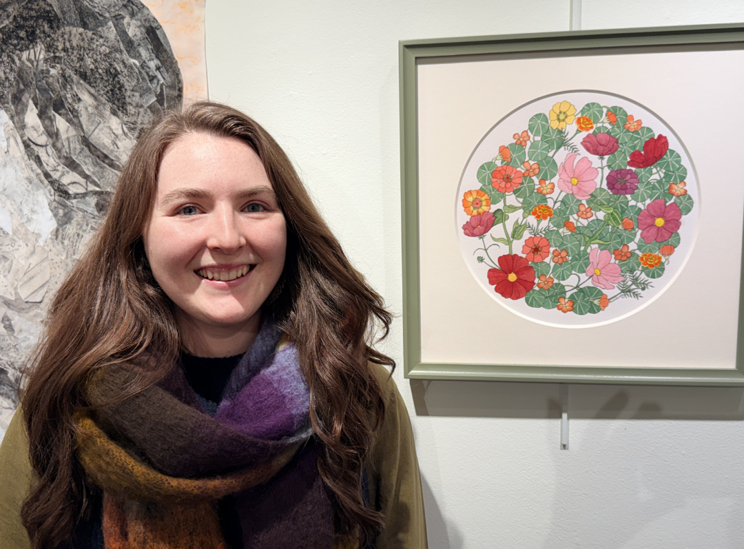 A smiling woman (Olivia) with long brown hair stands next to a colorful floral artwork in a gallery.