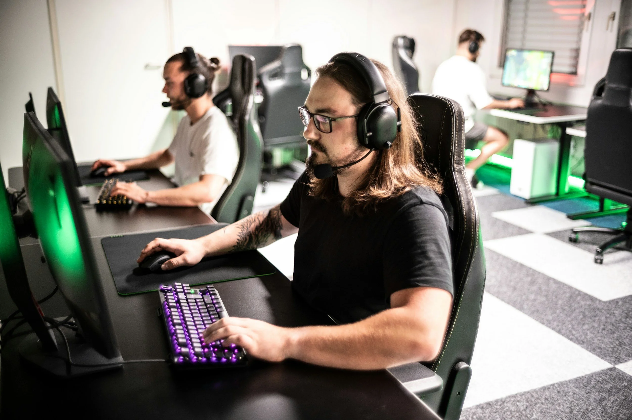 Gruppo di persone che giocano a videogiochi in un'arena di eSports, sedute davanti a computer con headset e tastiere retroilluminate.