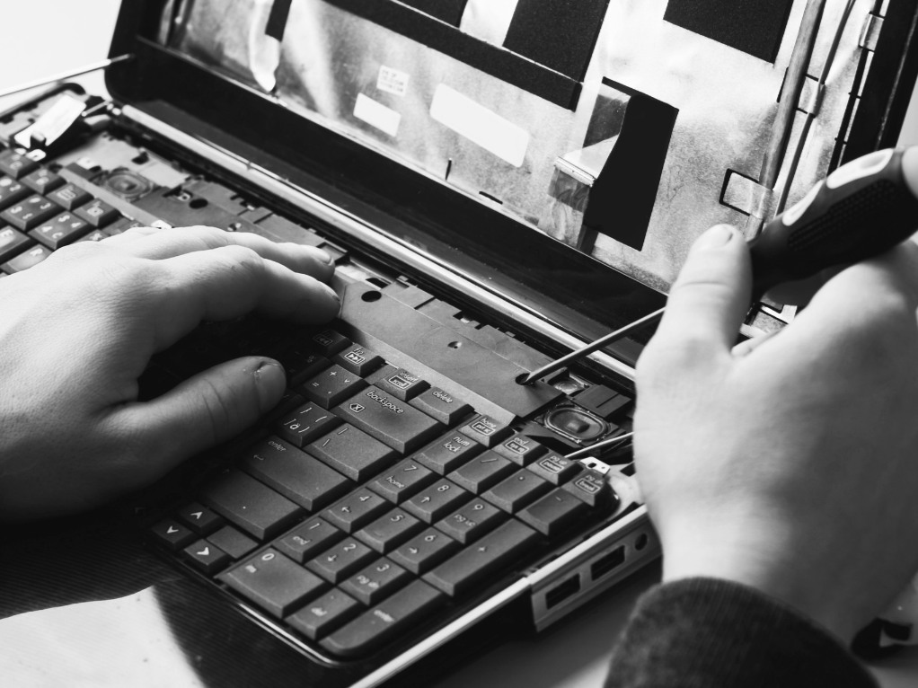 Una persona sta riparando un laptop usando un cacciavite, con la tastiera aperta e lo schermo rivolto verso l'alto.