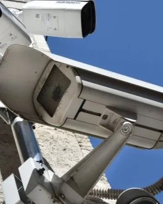 Telecamere di sorveglianza montate su un palo, con il cielo blu sullo sfondo.