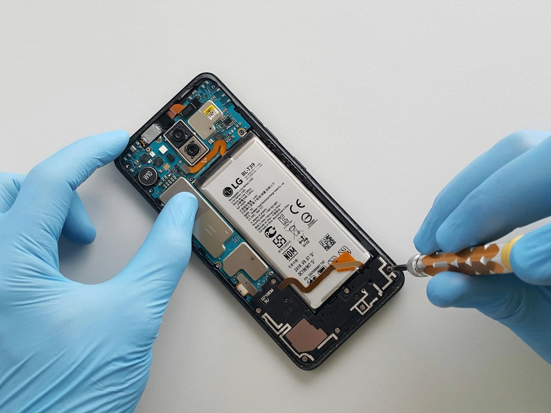 Un tecnico con guanti in lattice bluereballa uno smartphone, probabilmente per ripararlo o averlo smontato, nel background bianco.