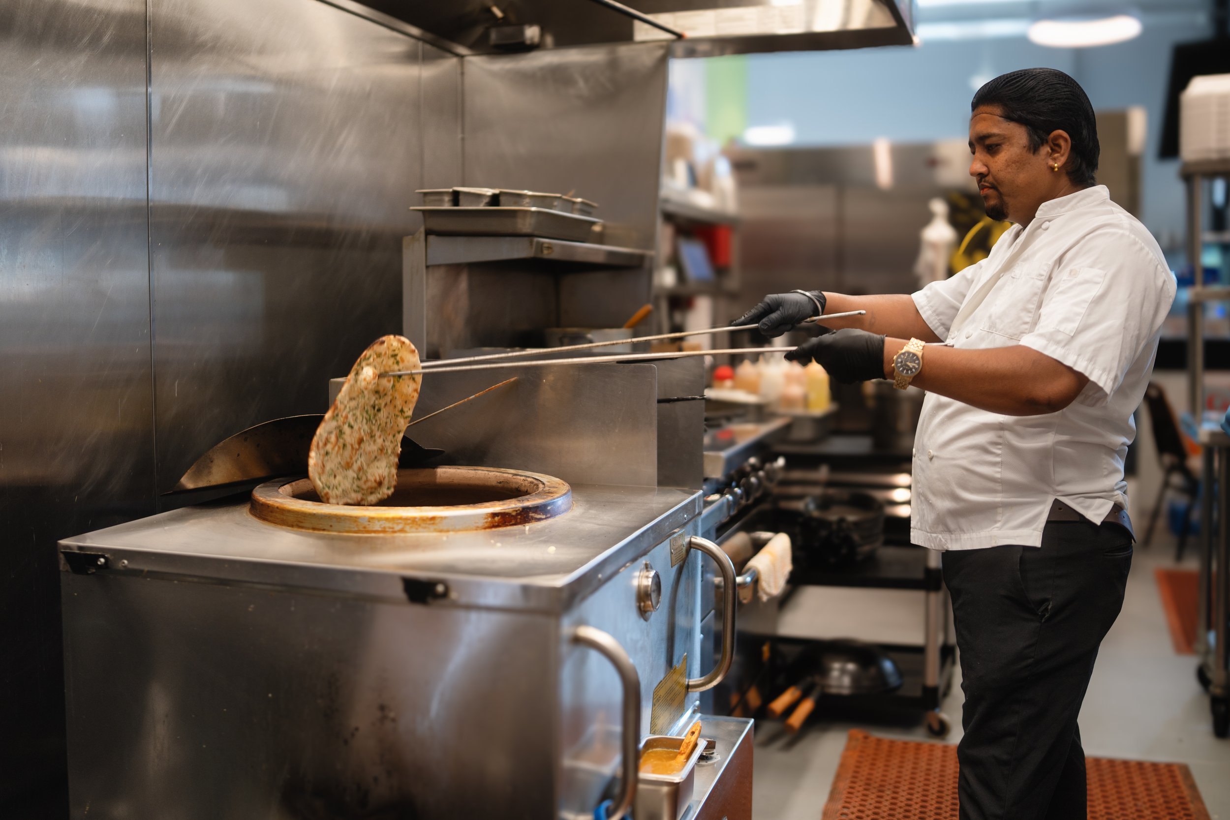 Chef using tandoor oven to cook naan bread in a commercial kitchen.
