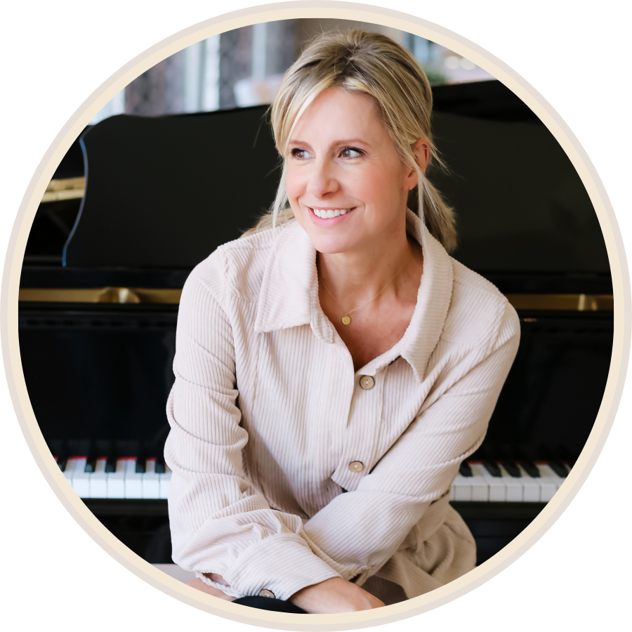A woman sitting at a piano with a smile, wearing a light-colored, long-sleeved shirt.