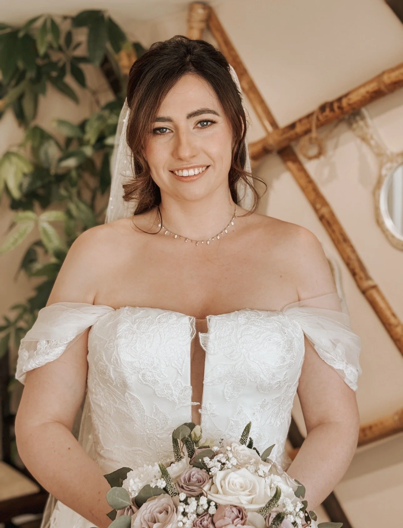 A smiling bride in a white off-shoulder wedding dress holding a bouquet of roses. In Ballymagarvey Village. Wedding Content Creator Ireland 