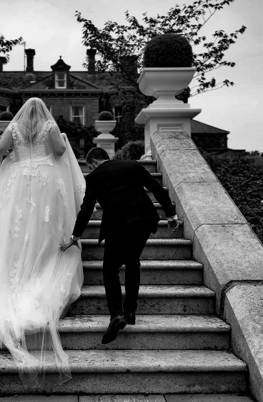 A bride and groom ascending an outdoor stone staircase in Tinakilly House, wedding venue. The bride is in a lace wedding gown with a veil, and the groom is in a dark suit helping her up the stairs. Wedding Content Creator Ireland 