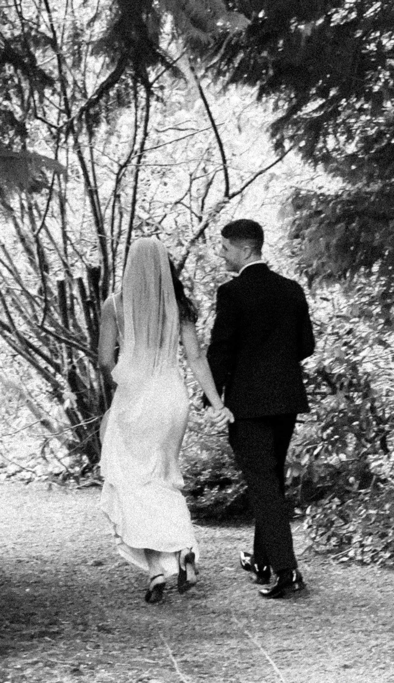A black-and-white photo of a bride and groom walking hand in hand on a forest path in Rathsallagh House, Co. Wicklow, wedding venue. Captured by Grey Acre Studios - Wedding Content Creator
