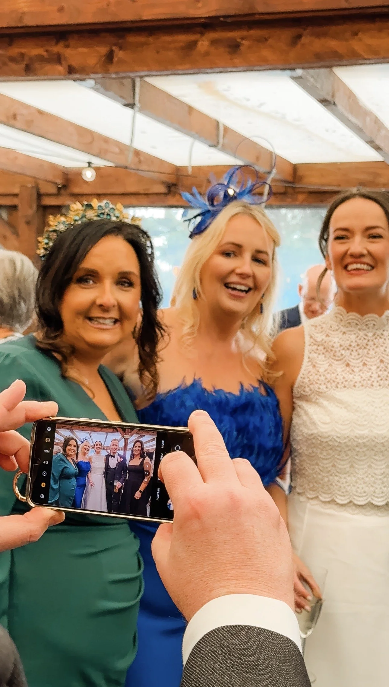 People at a wedding taking a group photo, with a person in a grey suit and white shirt in the foreground holding a phone, capturing the moment. Donegal Wedding Content Creator