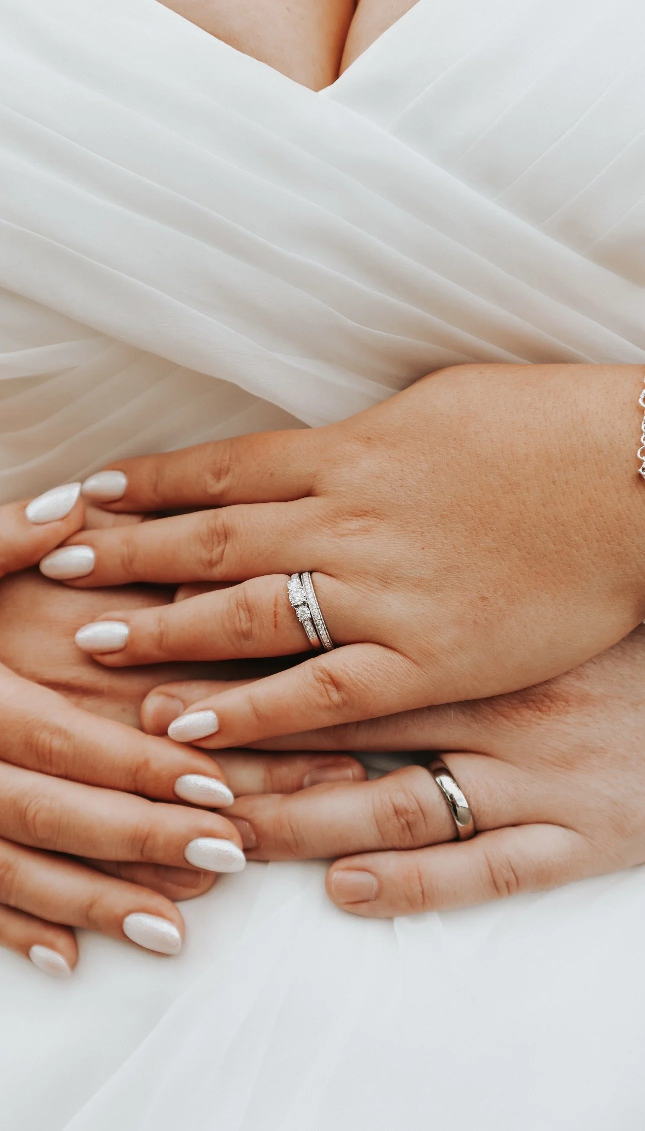 Close-up of a couples hands showing wedding rings and manicured nails, with a white, pleated fabric background. Wedding Content Creator - Grey Acre Studios in Mountain View Wedding Venue, Kilkenny