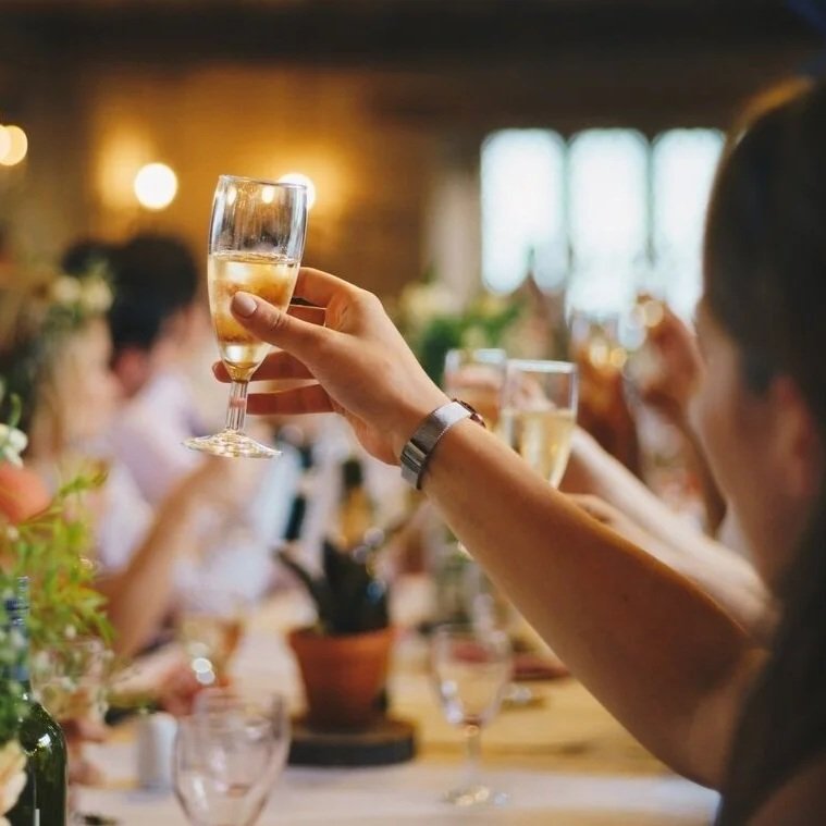 Person holding a glass of champagne during a celebration or gathering at a banquet.