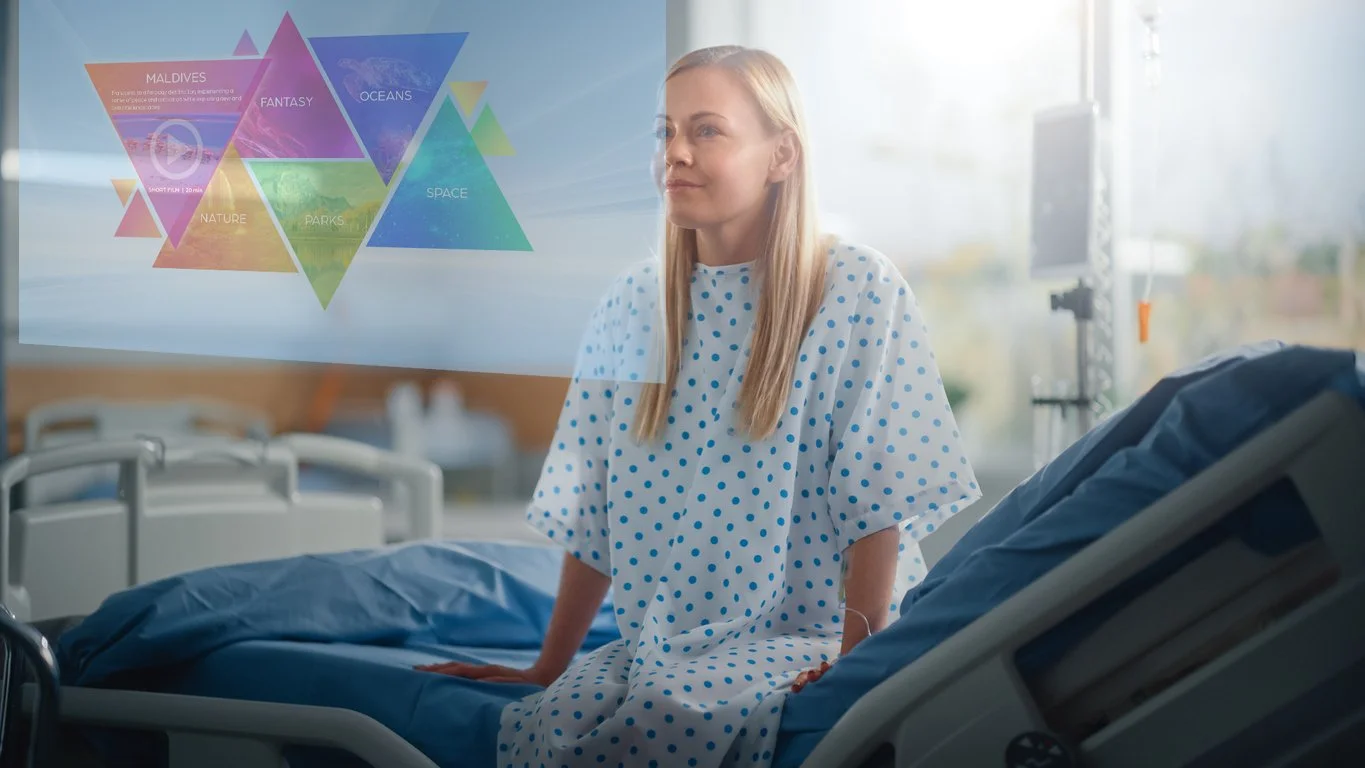 A woman in a hospital gown sitting on a hospital bed with her hands on the bed, looking at a transparent screen displaying colorful hexagons with words like 'Maldives', 'Fantasy', 'Oceans', 'Nature', 'Parks', 'Space', and 'South Lamu'.