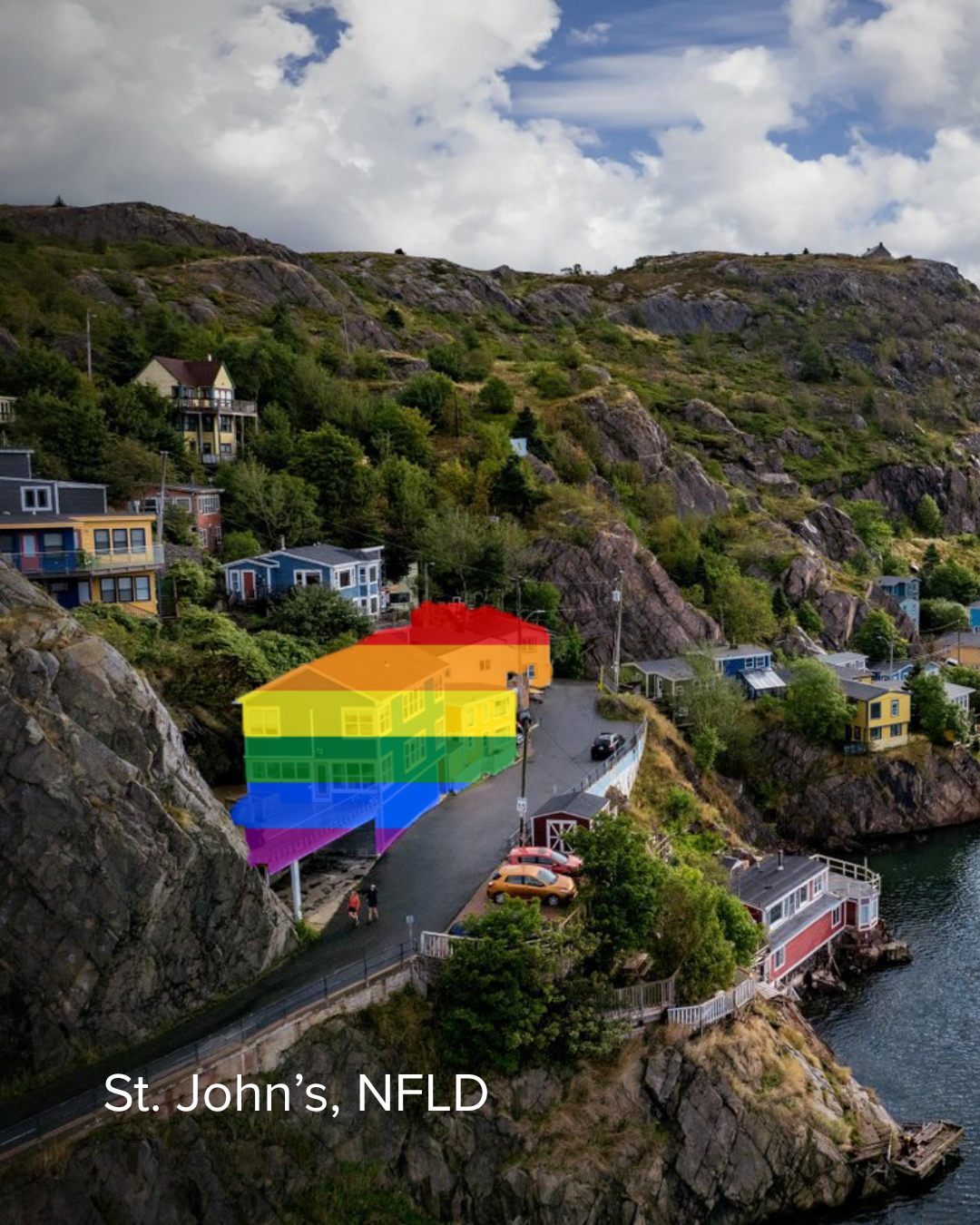 Houses along a coastal hillside with trees, rocky terrain, and water in St. John's, Newfoundland and Labrador. There is a rainbow pride flag overlayed on the buildings.