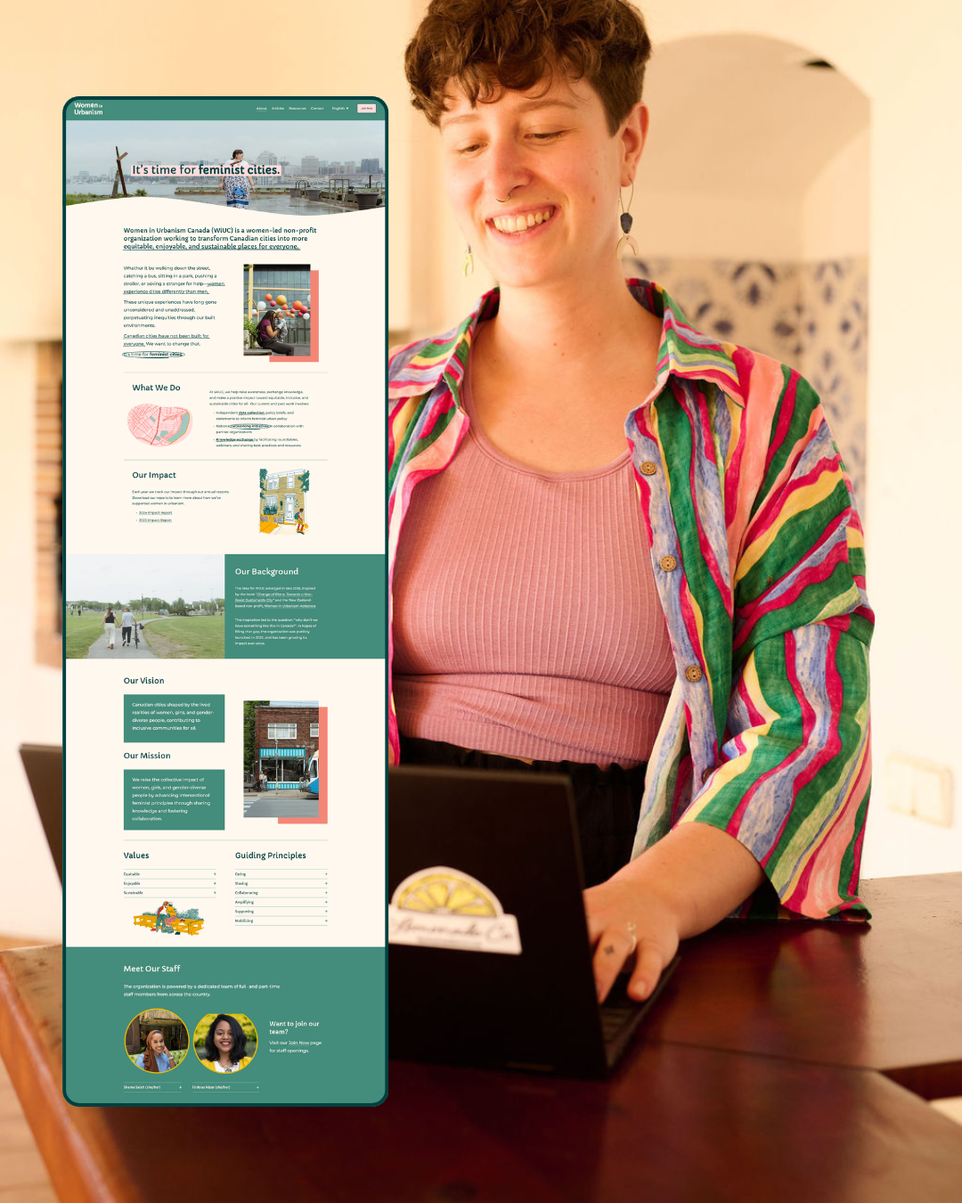 Meghan smiling while sitting at a table with a laptop. A large digital display floating in front of her shows a website for Women in Urbanism Canada.