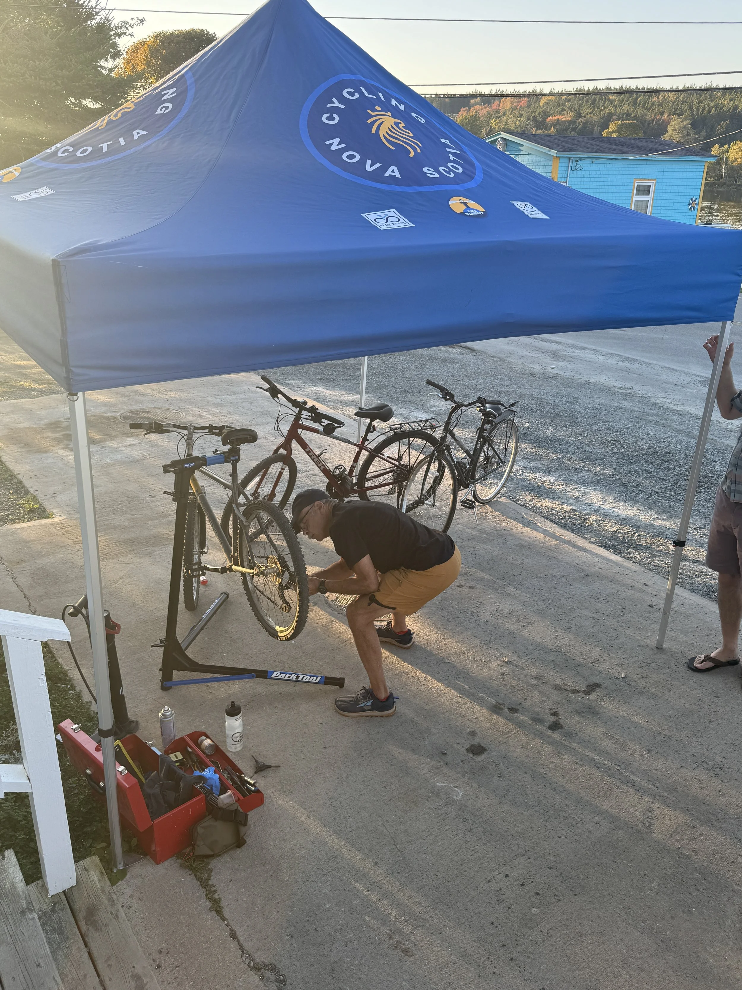 A person fixing a bicycle under a blue tent with the logo 'Cycling Nova Scotia'