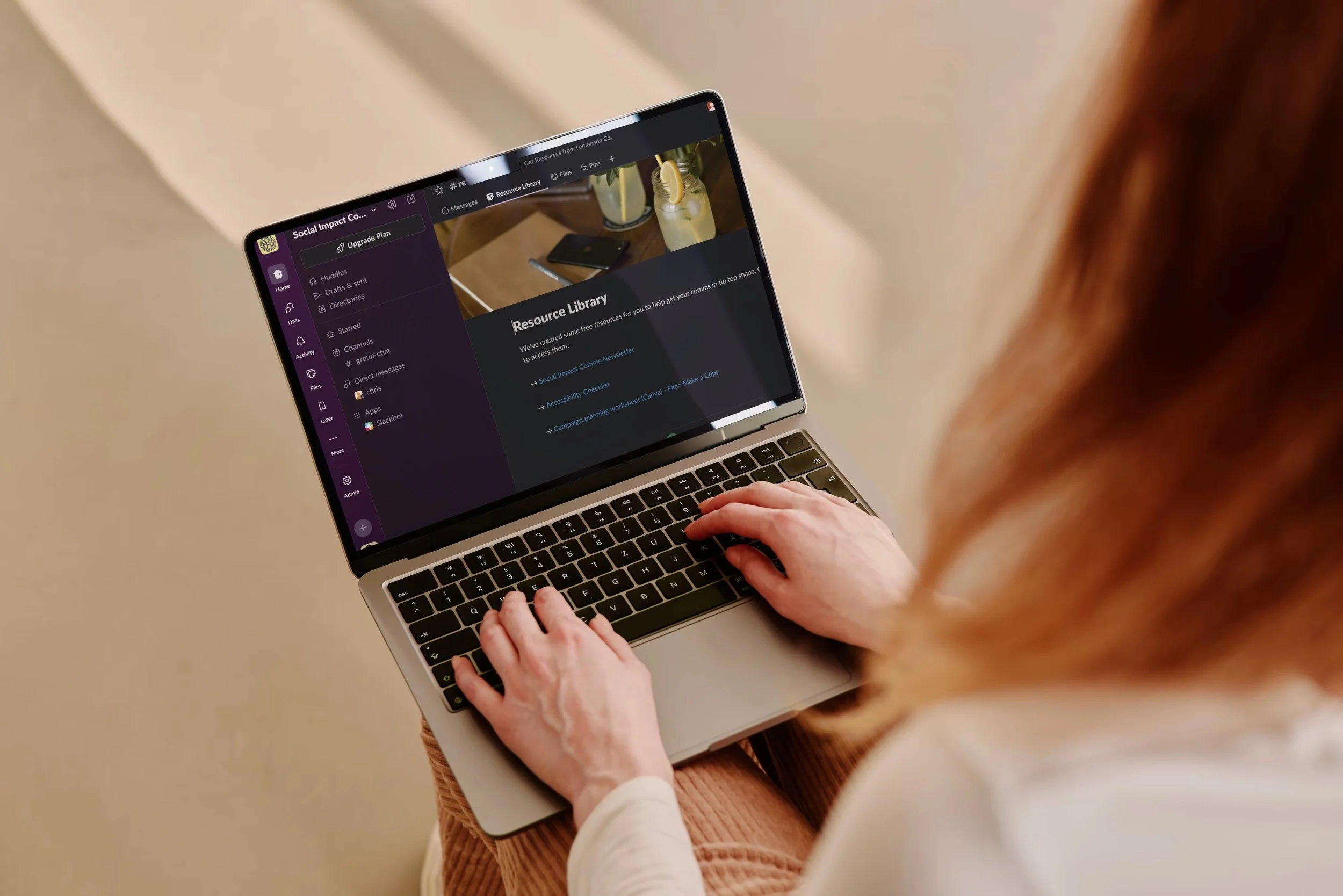 A person sitting with their laptop on their lap showing the Social Impact Comms Club slack community on the screen