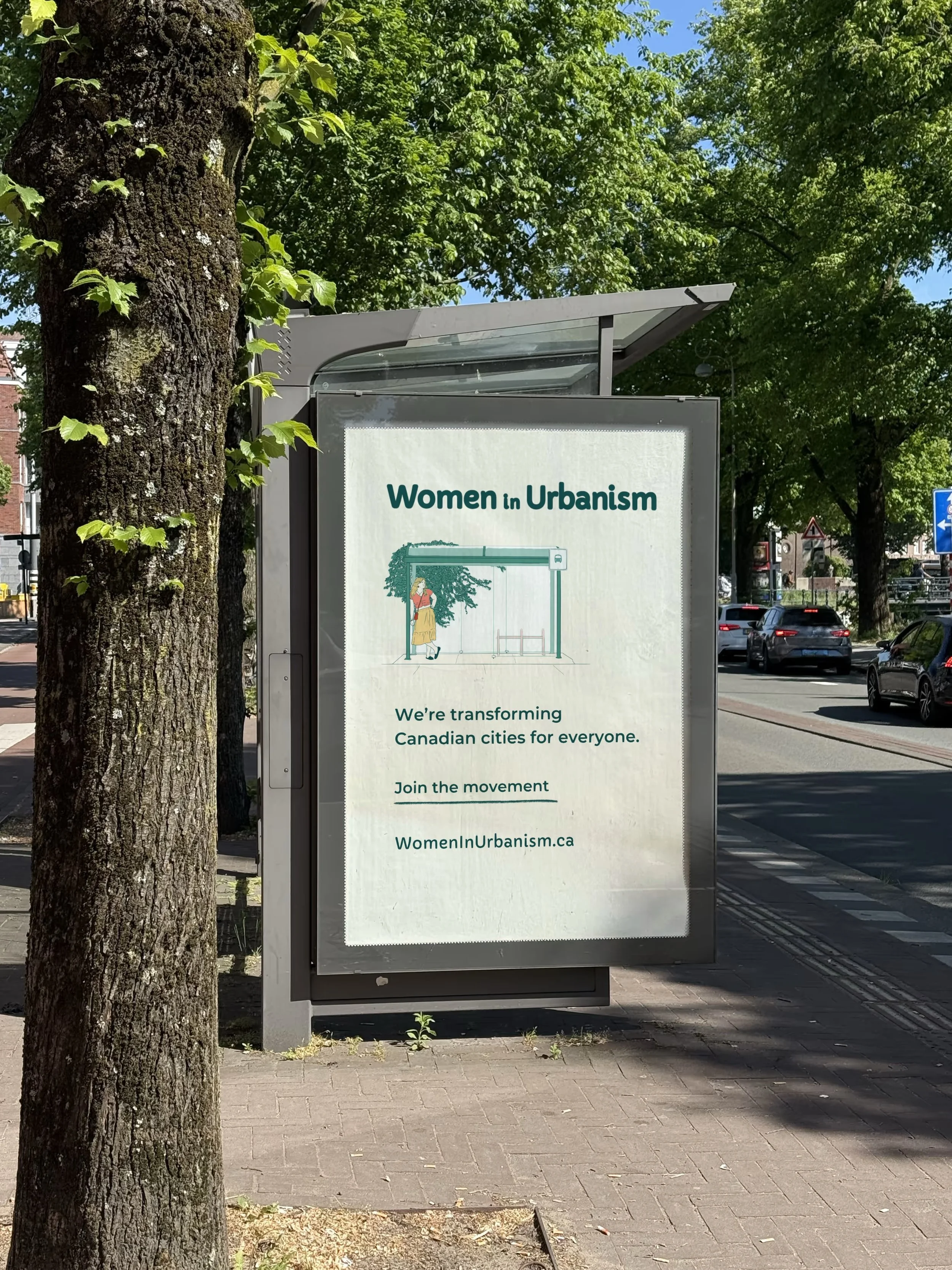 A poster titled 'Women in Urbanism' displayed on a bus shelter, with a drawing of a woman standing near a tree on a city street with cars and greenery in the background.