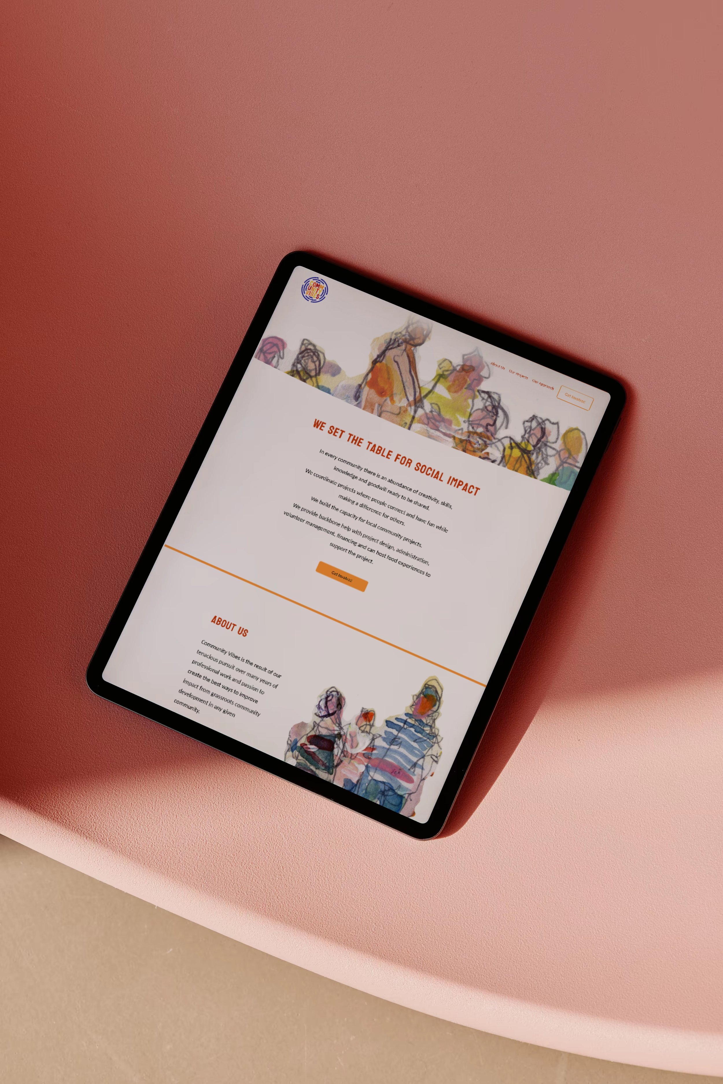 A tablet displaying a website with colorful abstract illustrations at the top and bottom, placed on a pink table. The website displayed was designed by Lemonade Co.
