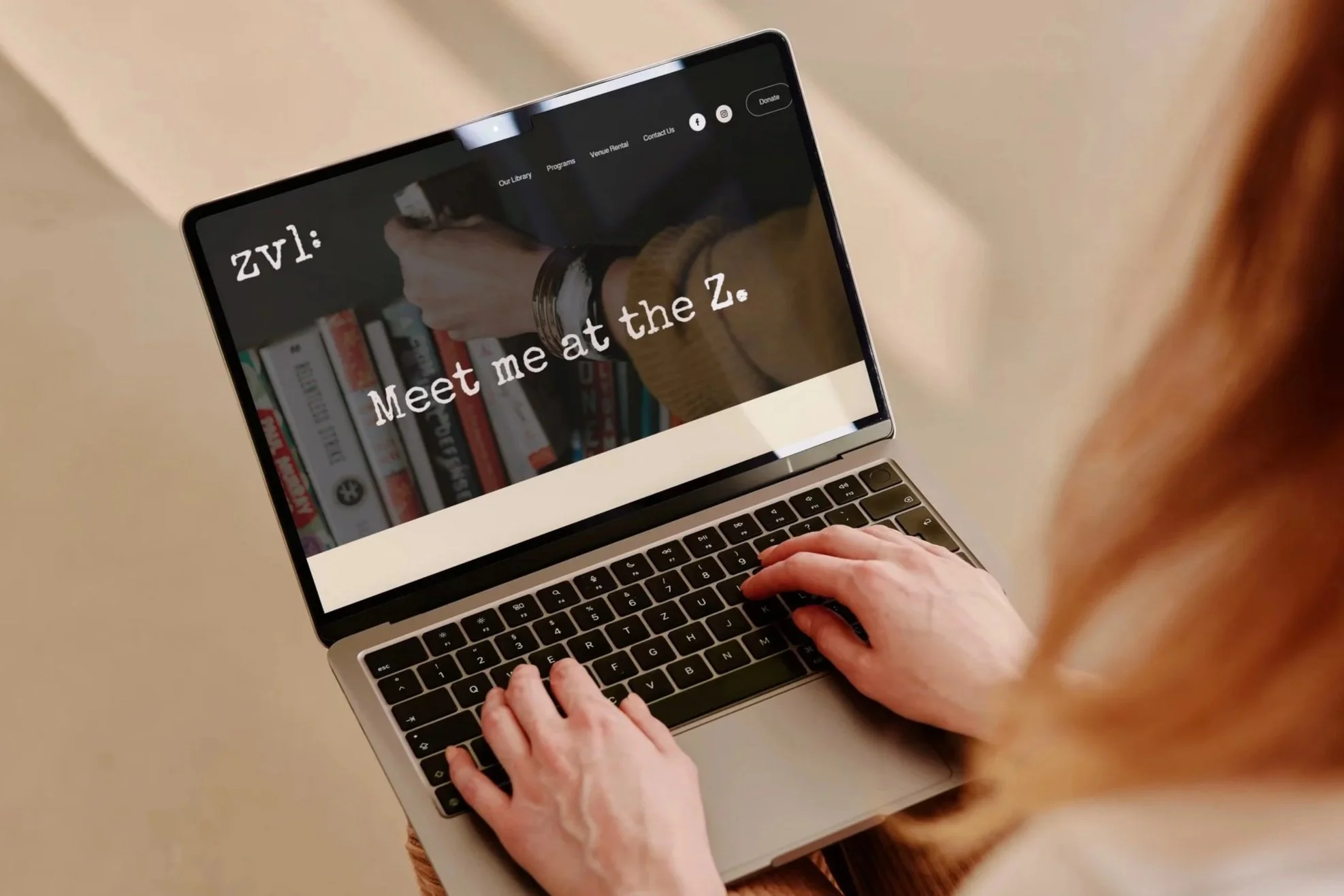 Person using a laptop with a website open that says "Meet me at the Z." and shows a hand reaching for a book.