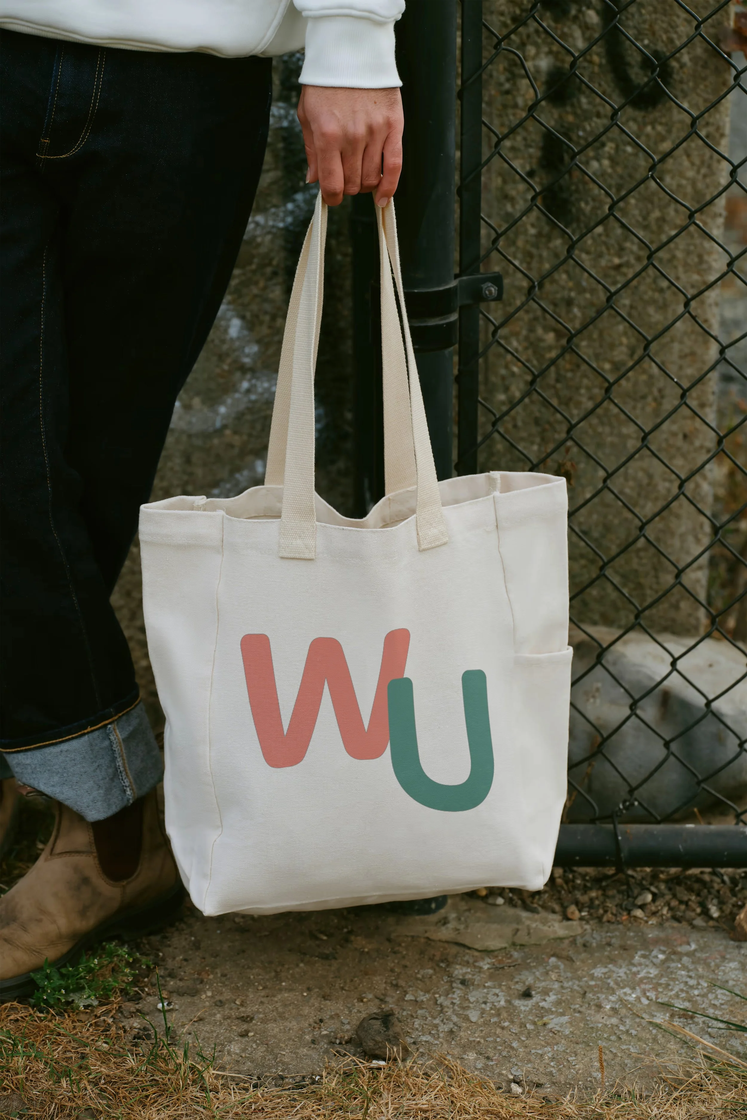 Person Blundstone boots and black jeans standing next to a large tote bag with the letters 'WU' on it, which is short for Women in Urbanism Canada.